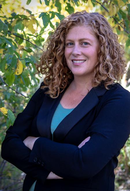 Amber Shanklin posing for a headshot photo. Taken outside in front of a lot of trees.