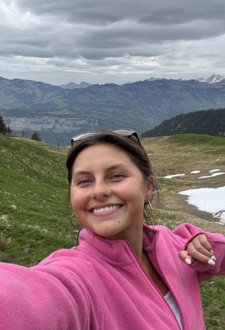 Sofia in a pink sweater posing for a photo with a mountain backdrop. 