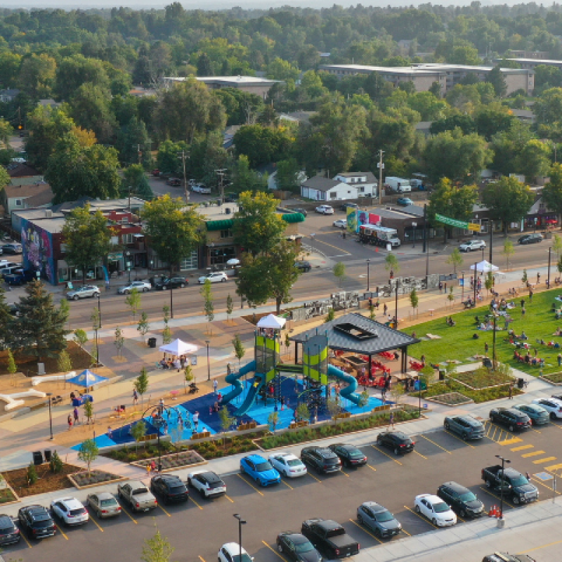 Aerial shot of a new park with a playground and open grassy lawn in a neighborhood surrounded with trees. 