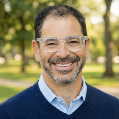 Headshot of a man with clear glasses in a blue sweater smiling for a photo.