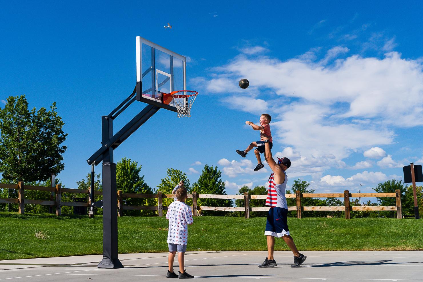 Parent holds child up to shoot a basketball into the hoop.