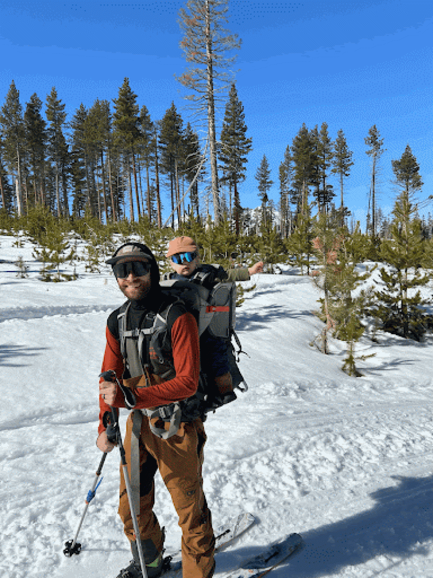 Father and child on a backpack carrier during a snowy hike.