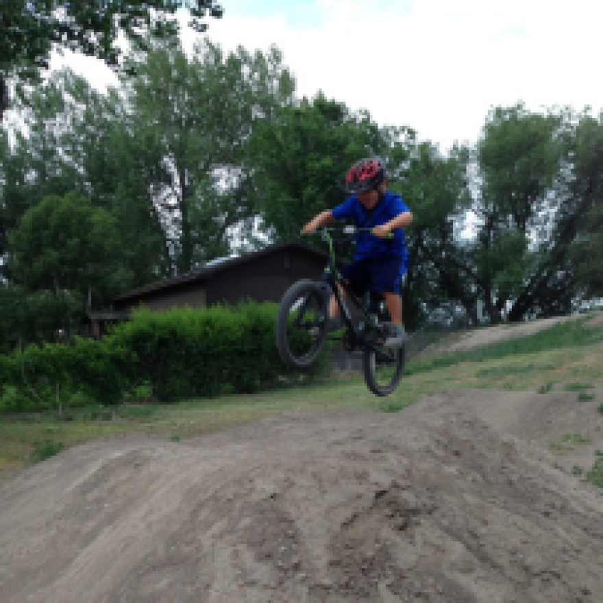 Small child on a bike performing a jump off a dirt hill. 